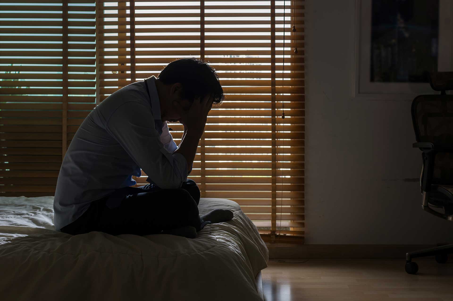 Future Search Trials Depression Study in Dallas. Man covering his face while sitting on bed in dark room.